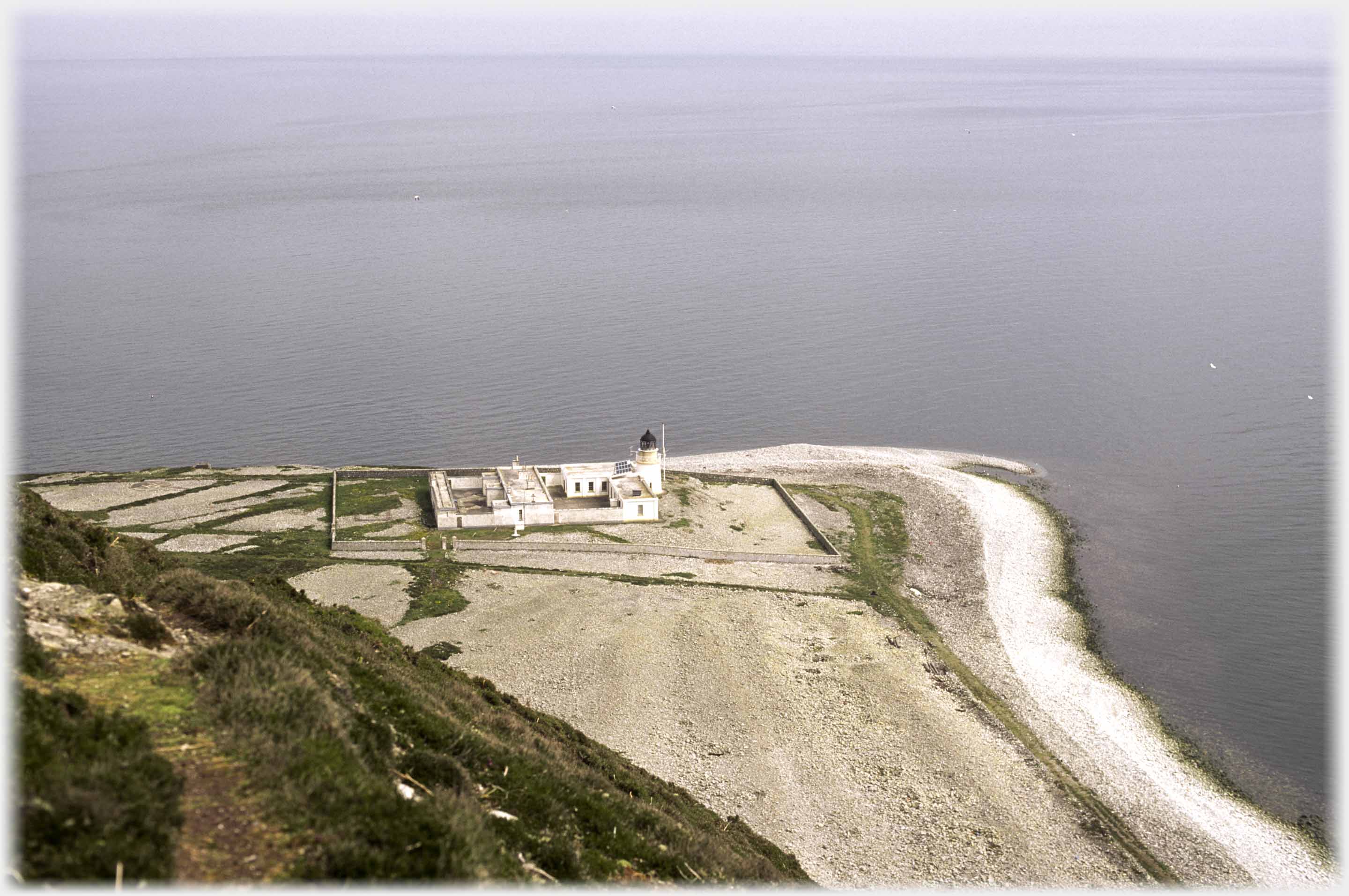 Looking over the lighthouse across the sea to thin line of shore.