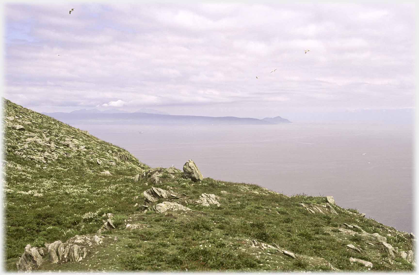 View across hillside to projection of land across sea, humped at the end.