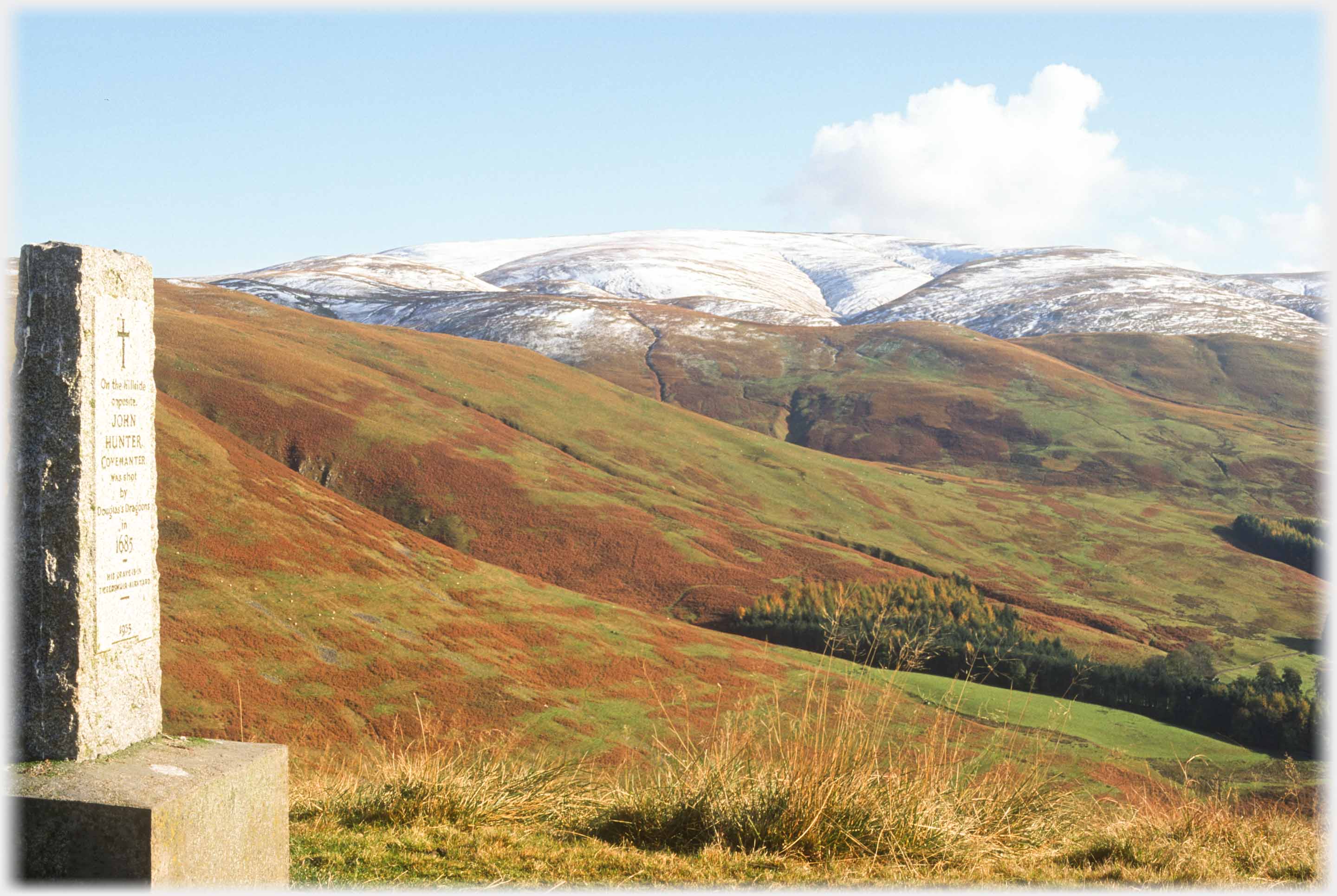 Granite monument side with hills rising to main snow covered top.
