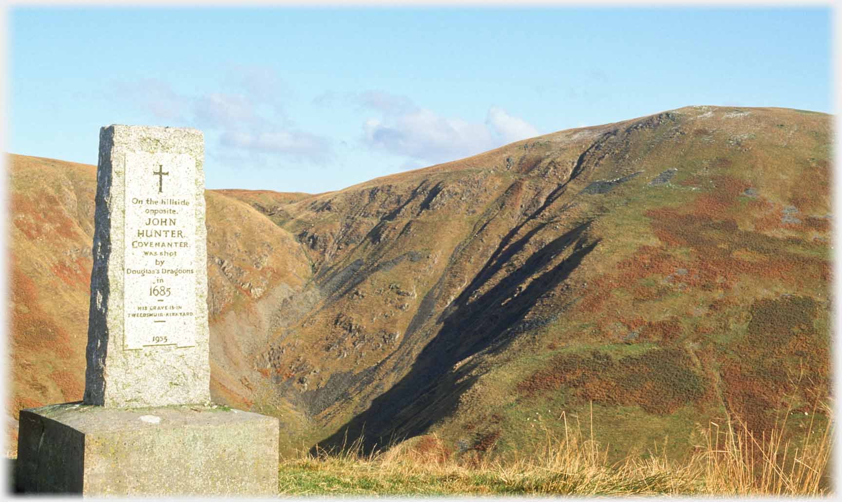 Granite monument face, steep shodowed hills beyond.