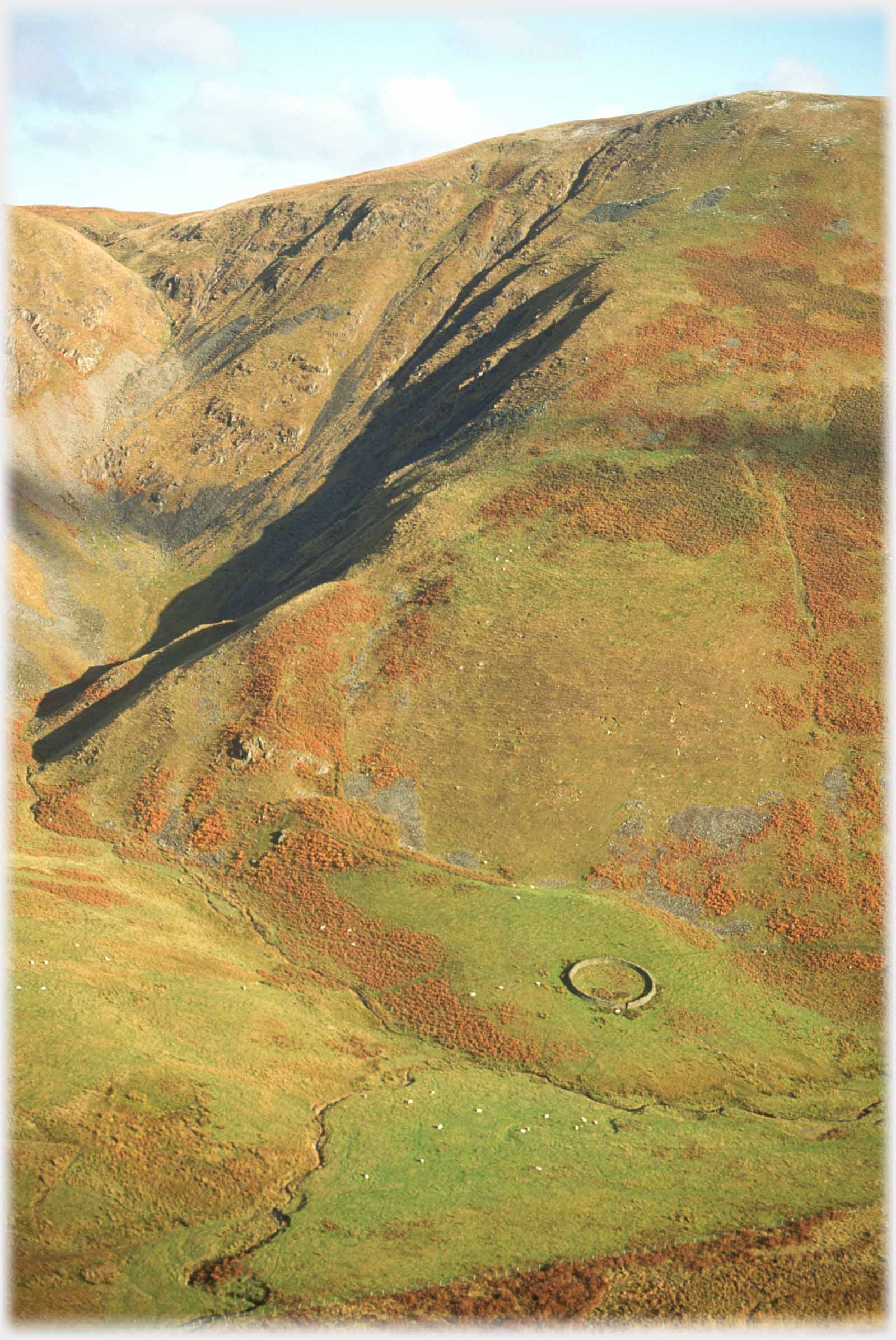 Broad hillside with scree to left and sheep circle at base.