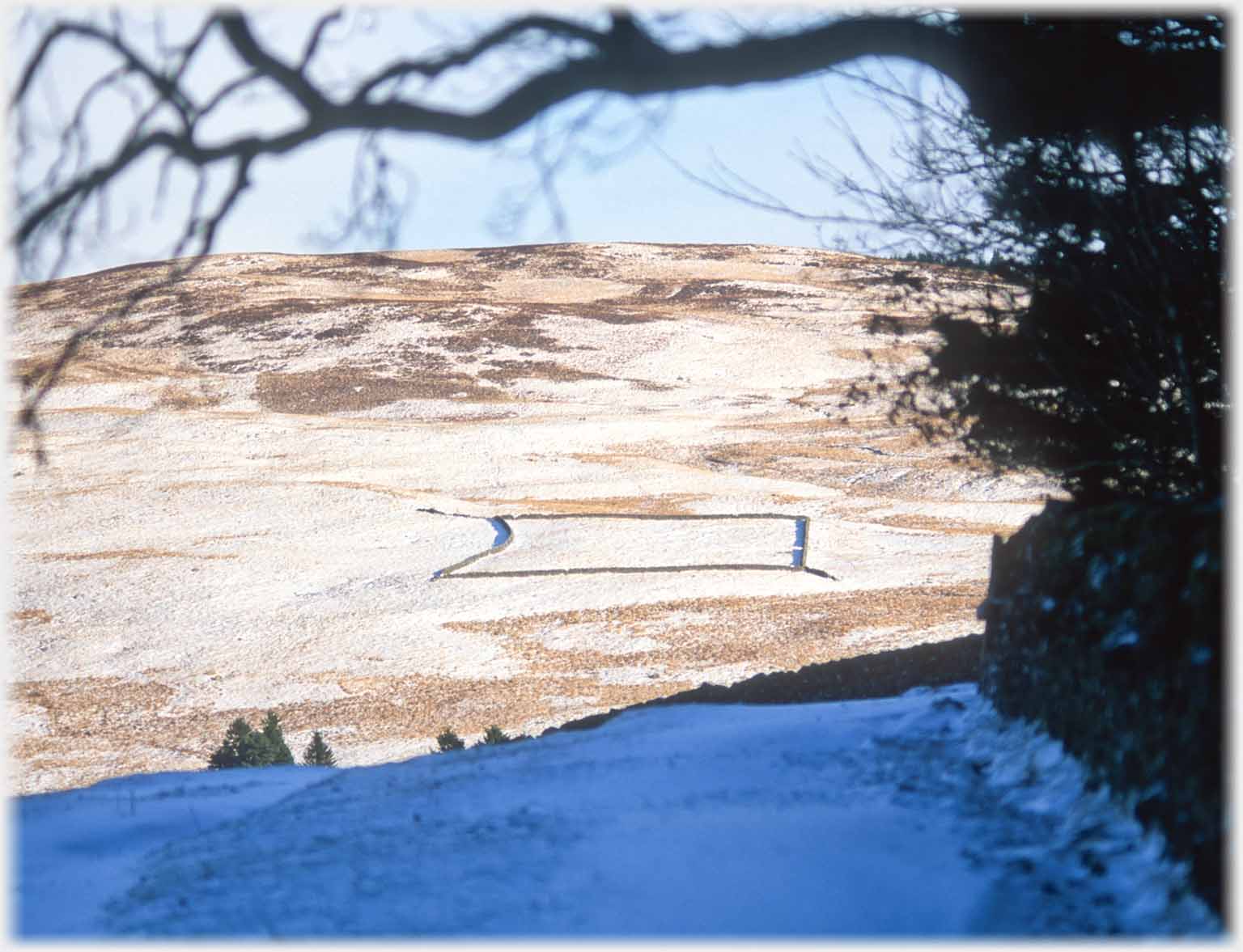 Large square dyke on snow sprinkled hillside.