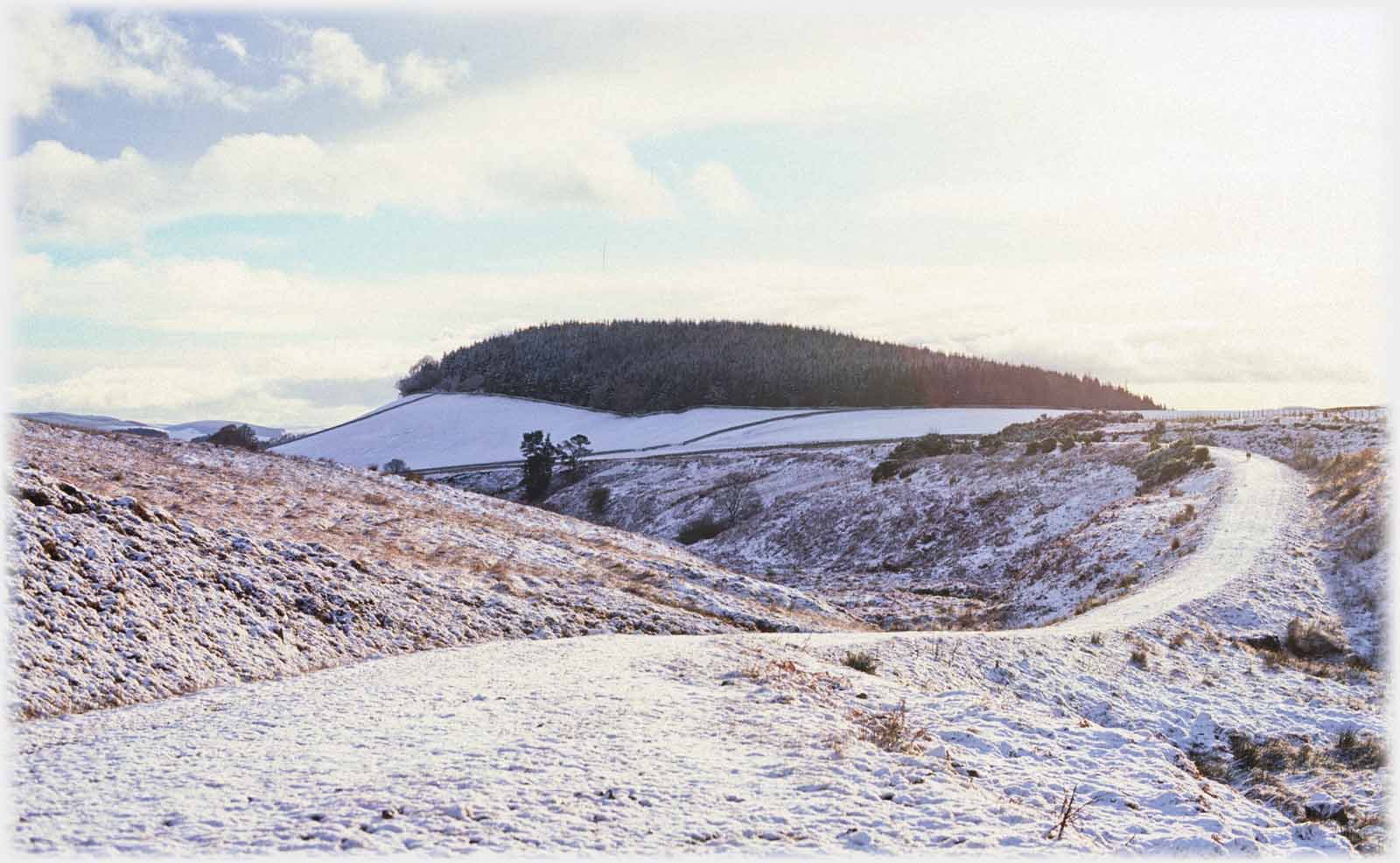 Raised track running towards hill with light snow covering.