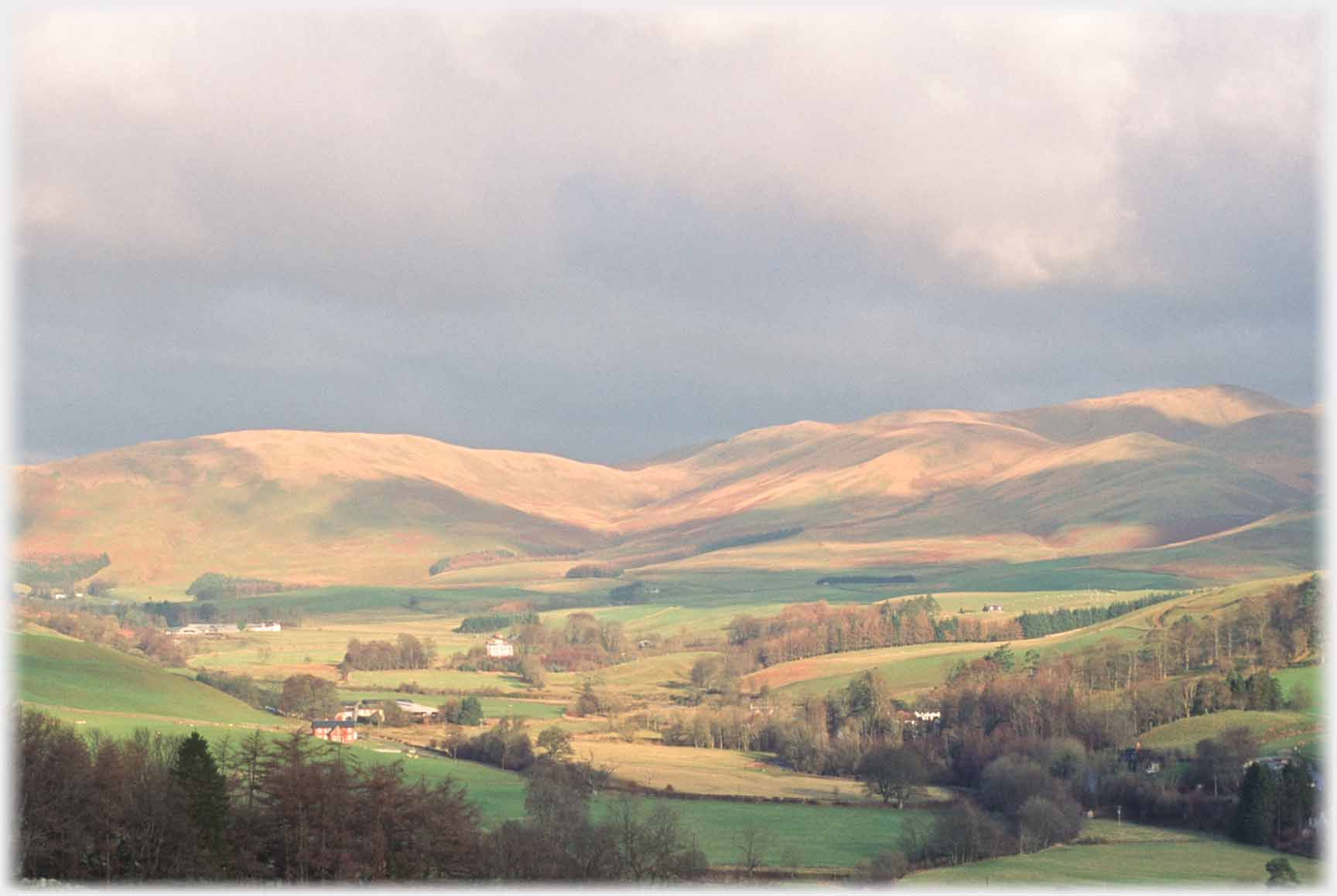 Treed valley with hills beyond mostly in sunlight.