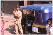 Driver holding child standing beside his auto.