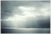 Heavy grey sky with shafts of sunlight hitting the sea.