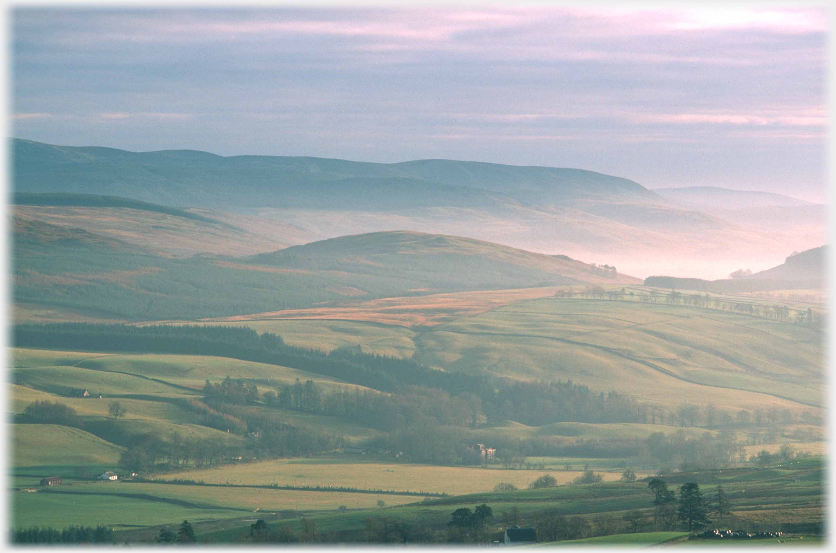 Central gentle domed hill with mist around it and hills beyond.