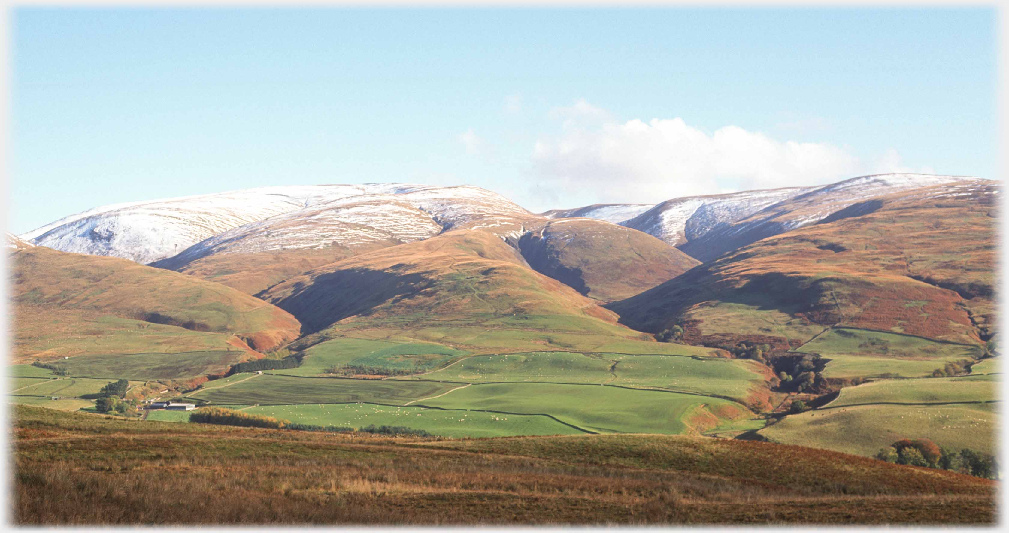 Looking across the fields of the upper Annan Valley at lightly snow covered hills.
