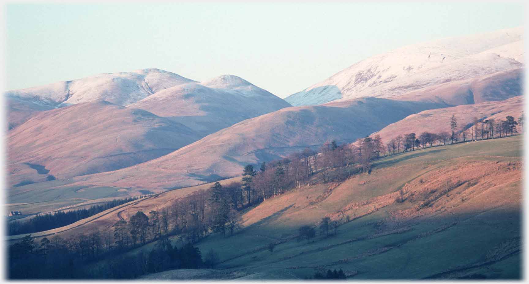 Hills behind hills in sunset with snow on tops.