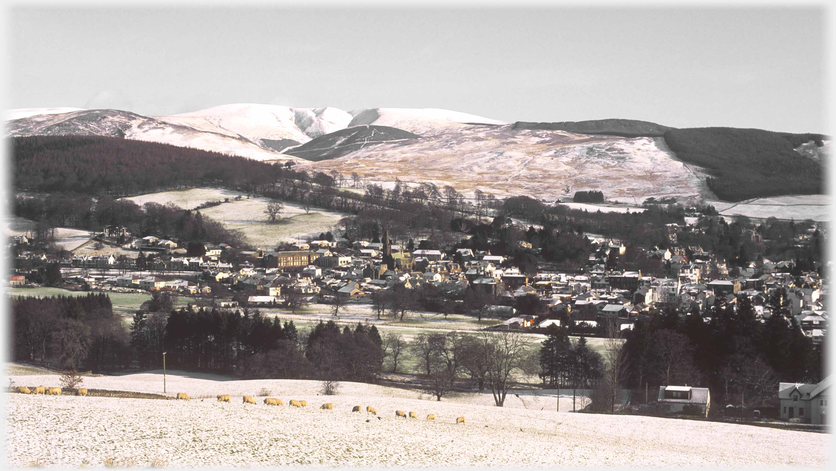 A dark drown townscape with snow covered hills beyond.