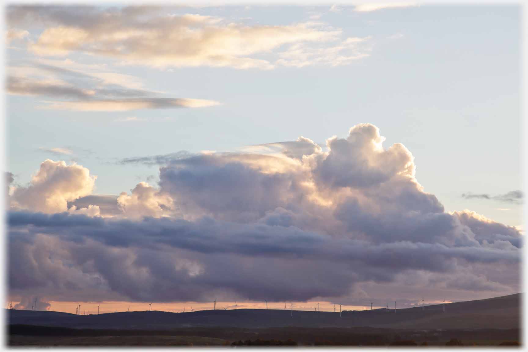 Heavy dark cloud sitting on slit of light peppered with turbines.