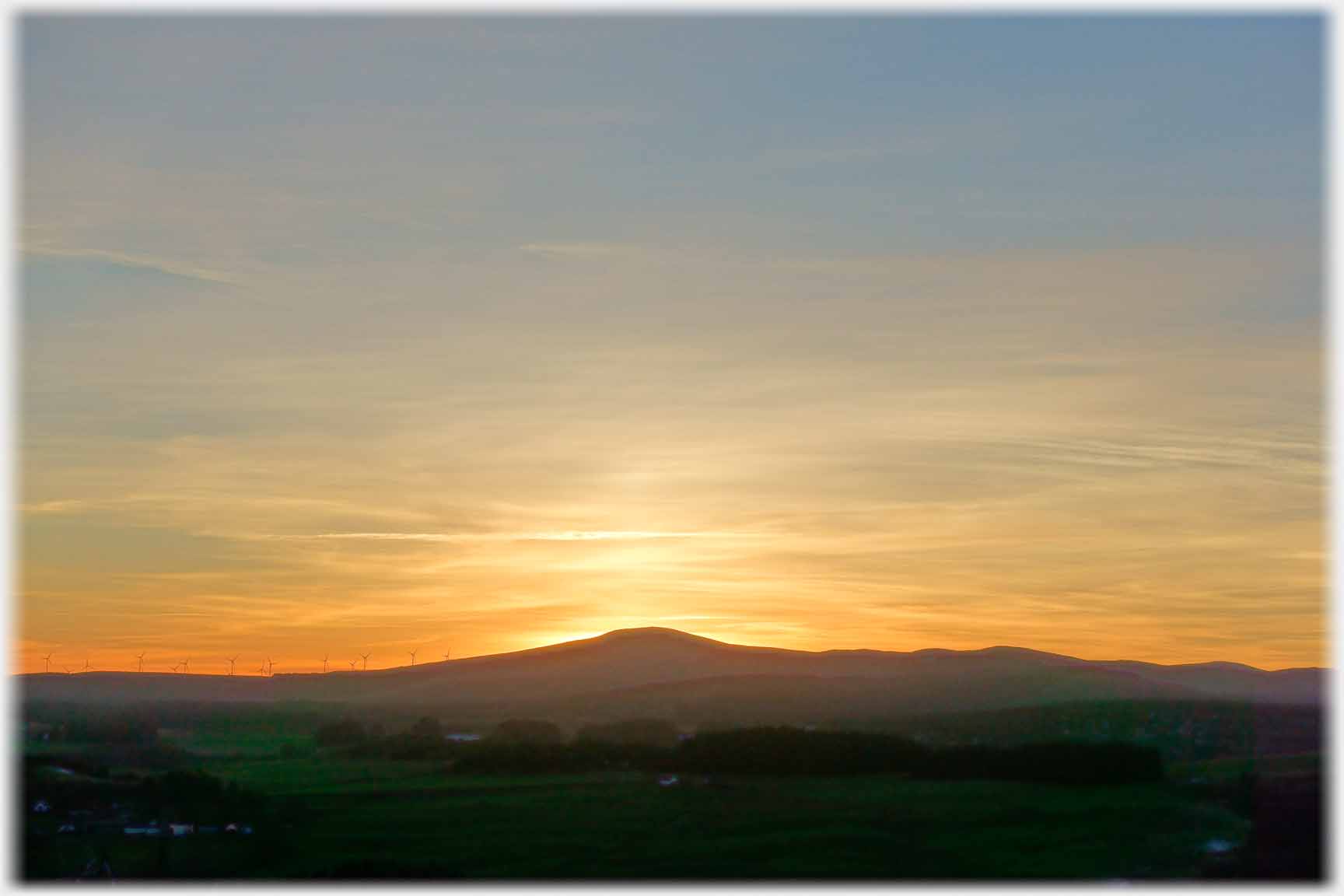 Volcano shaped hill with setting sun directly behind.