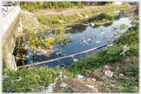 Small river with much rubbish round and in it.