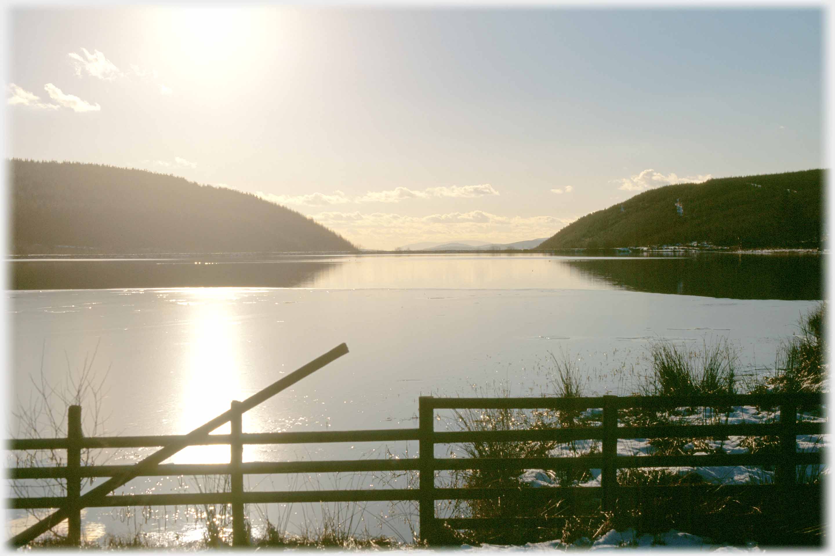 Loch half covered in ice, and foreground fence.