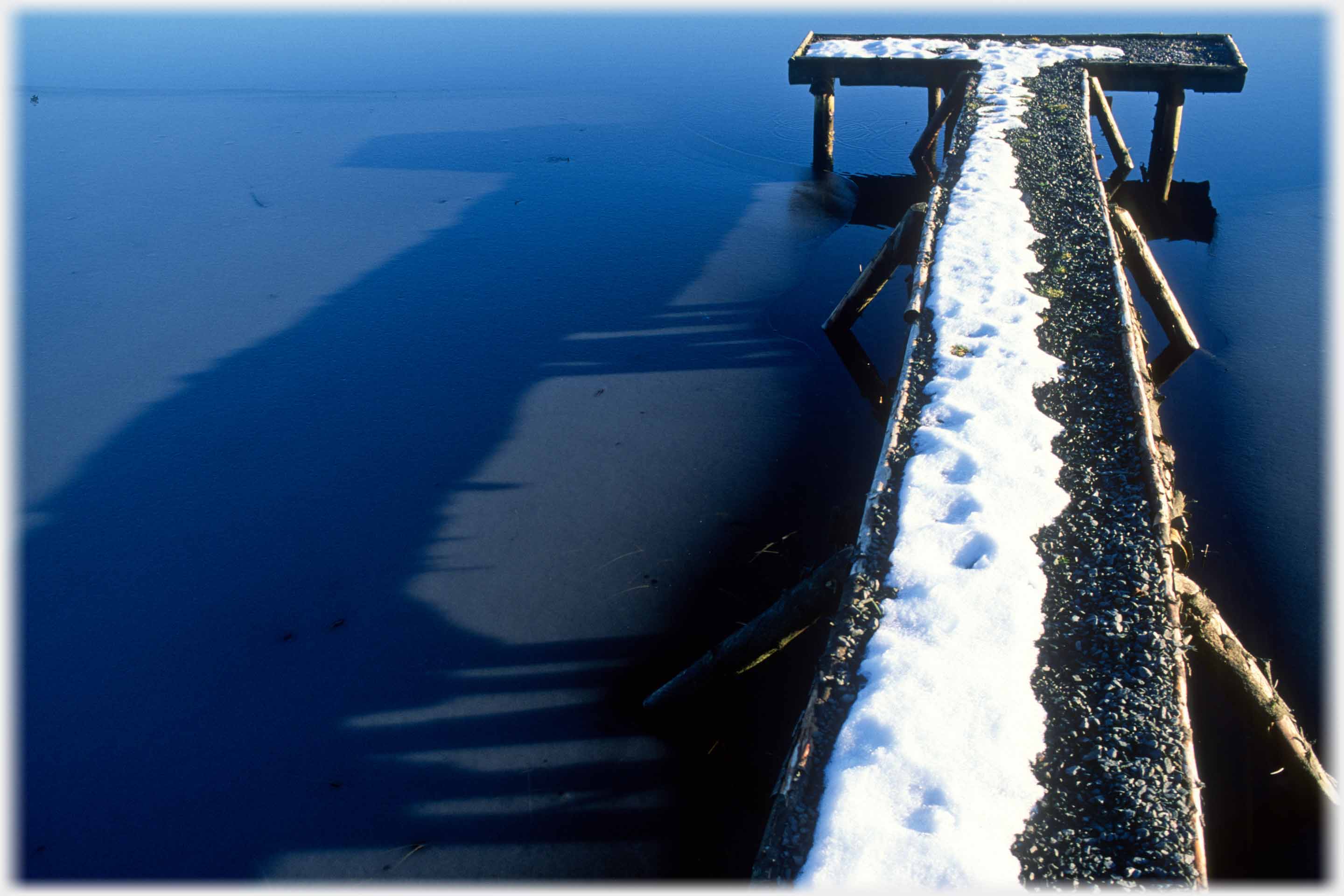 Pier widening into T-shape casting a long shadow.