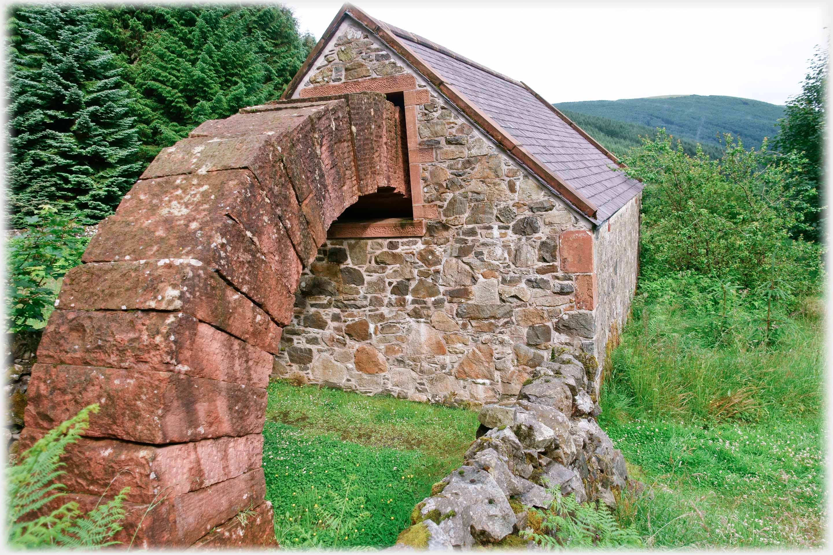Red stone arch curving up from the ground and into a barn through a window.