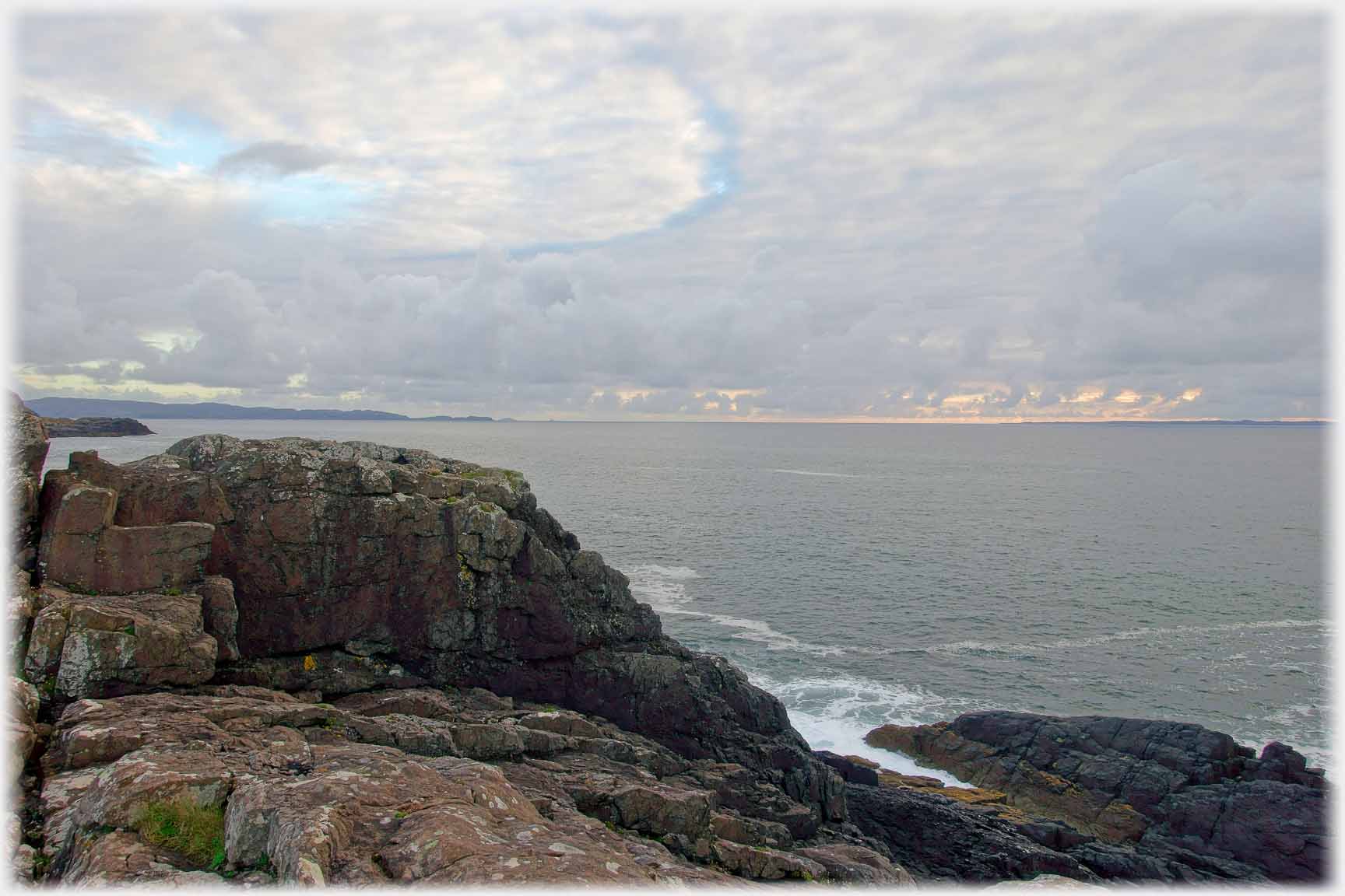 Rocks, clouds, sea and distant land.