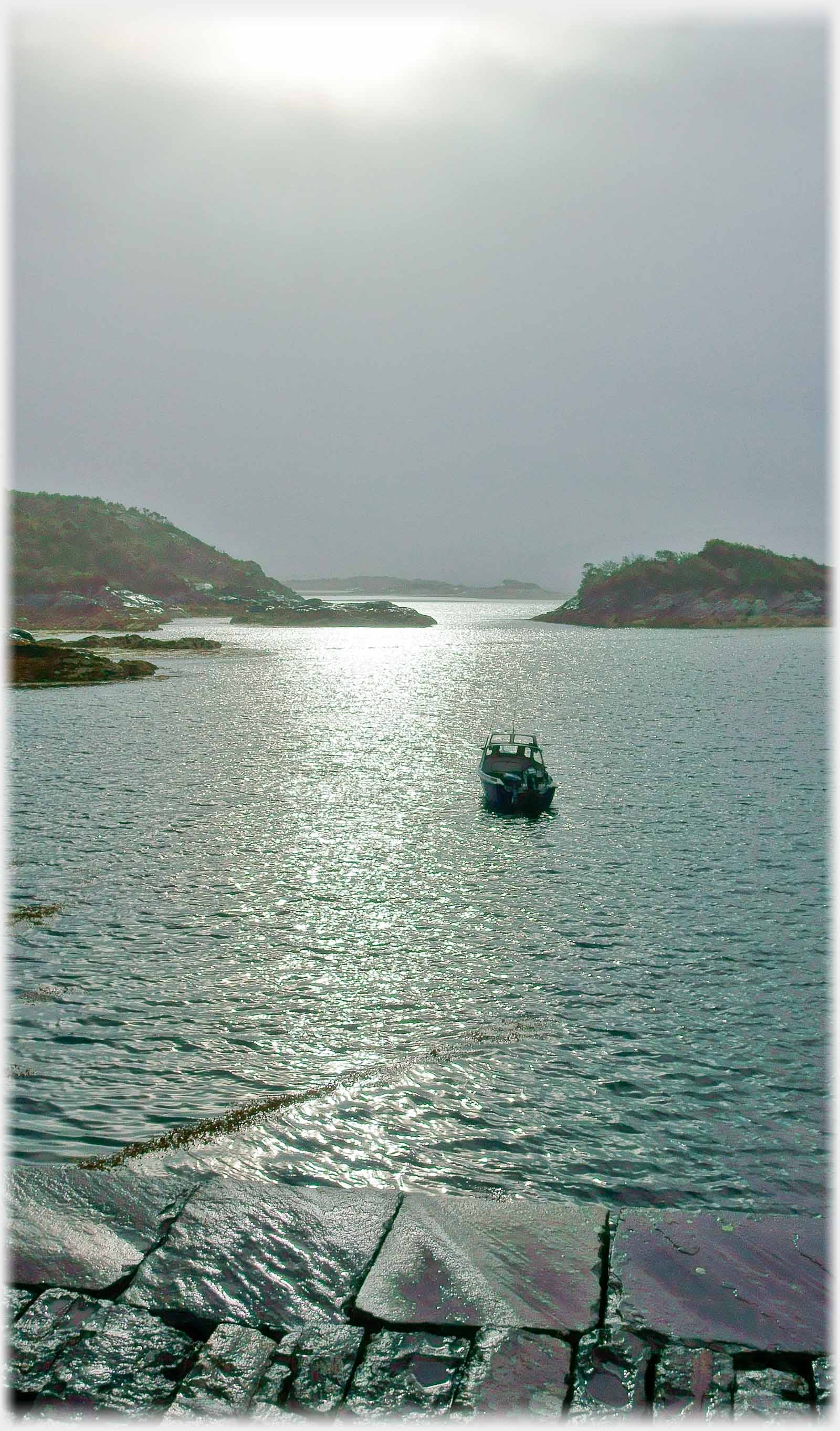 Edge of pier with boat on sun reflecting water.