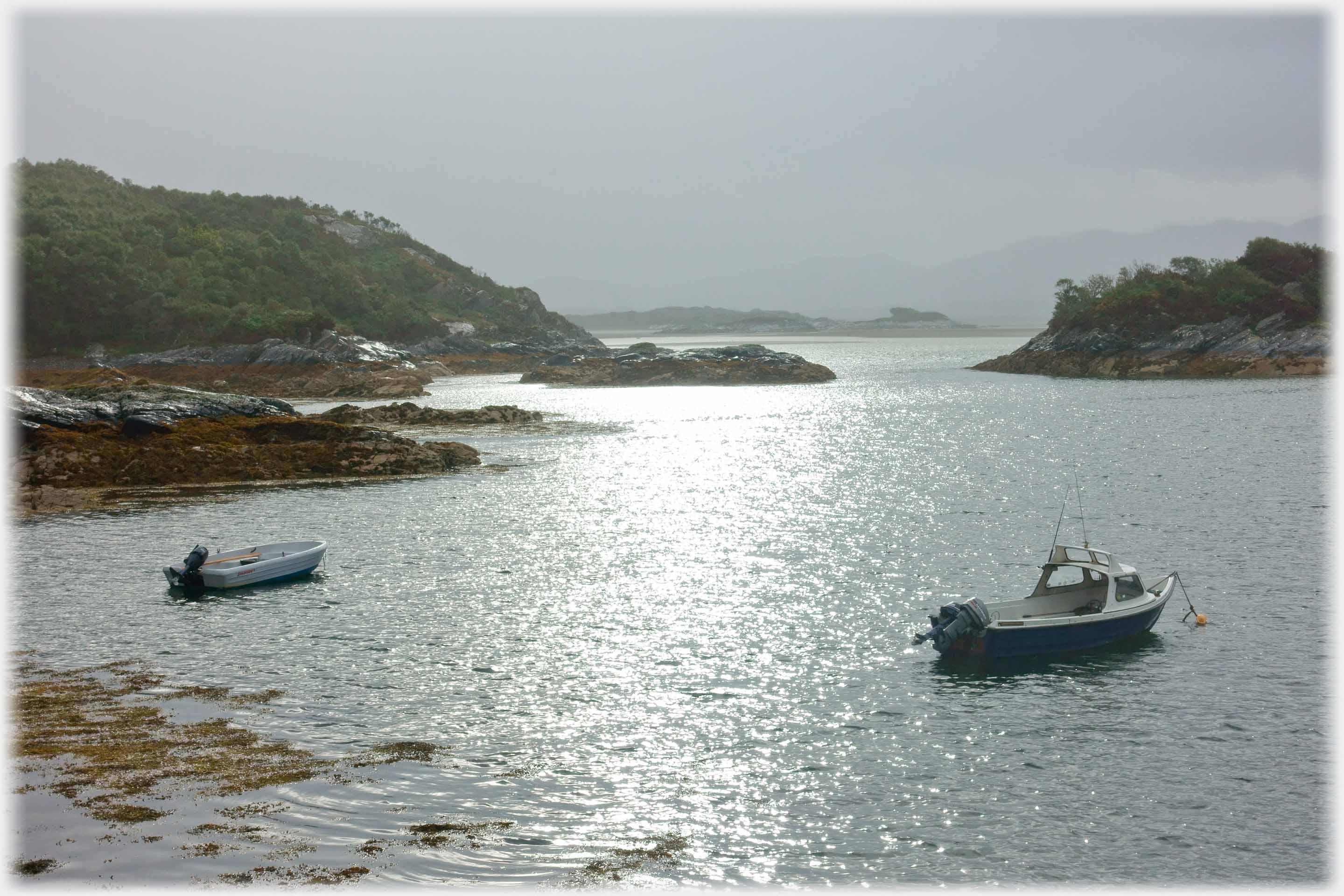 Sea bay with two boats and reflected sun.