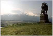 Monument with three figures looking towards snowswept mountains.