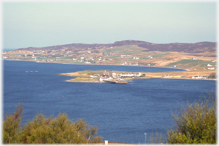 View of the village arrayed along the loch side in sunlight.