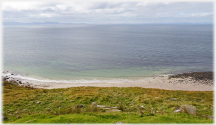 Sandy bay with turqoise edged sea and distant slither of land.