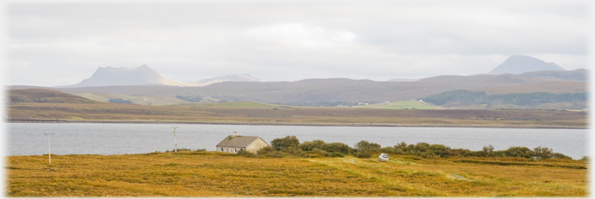 Bungalow by loch with separated hills beyond.