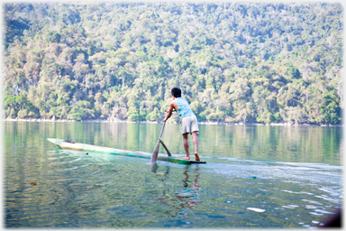 Man leaning on his paddle and producing a wake behind the boat.