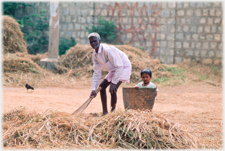 Grey haired man sweeping with small child standing beside large basket.