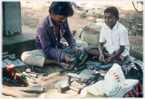 Cobbler sitting with tools of his trade on the ground with a boy.