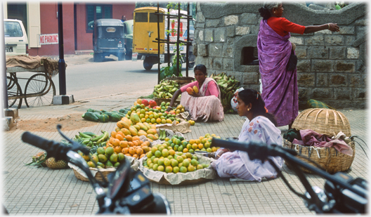 Two women on ground with piles of fruit.