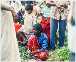 Well dressed woman on ground beween piles of vegetables.