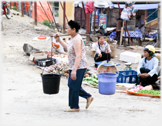 Woman with panniers and street vendors.