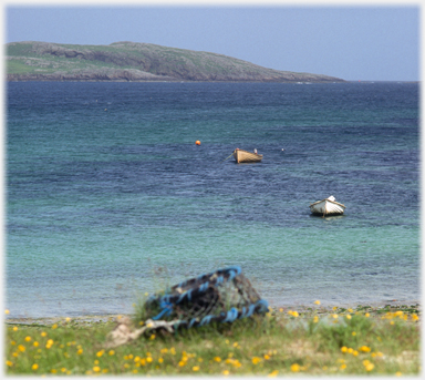 Loch with boats and a creel on the shore.