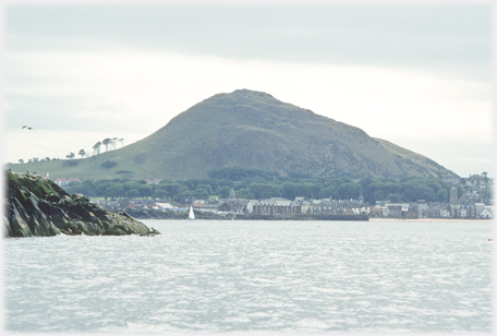 View of hill from sea with houses along shore.