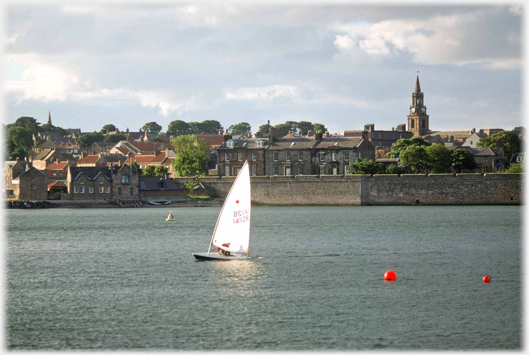 Sailing dinghy with town buildings behind.