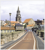 Looking across a narrow bridge to huddled roofs.