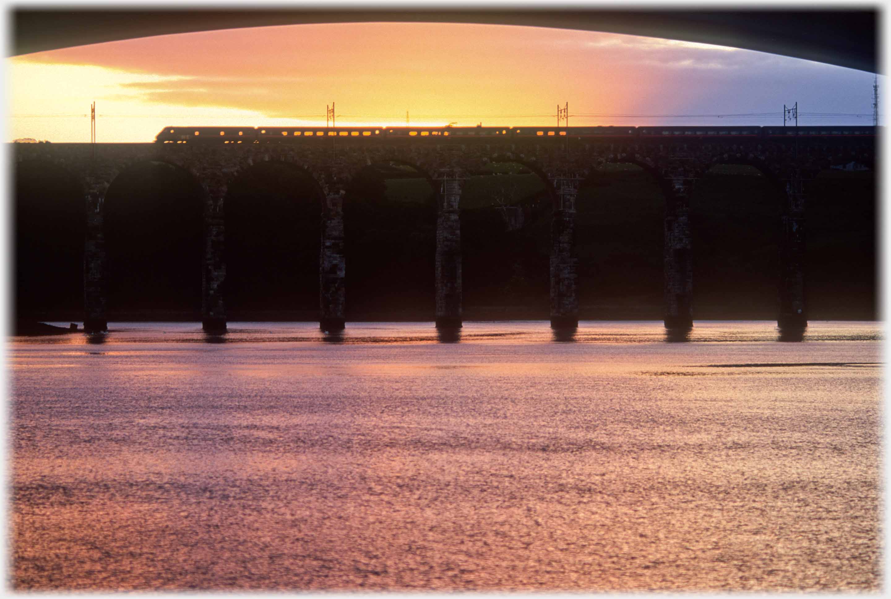 Silhouette of bridges in sunset with train passing over.
