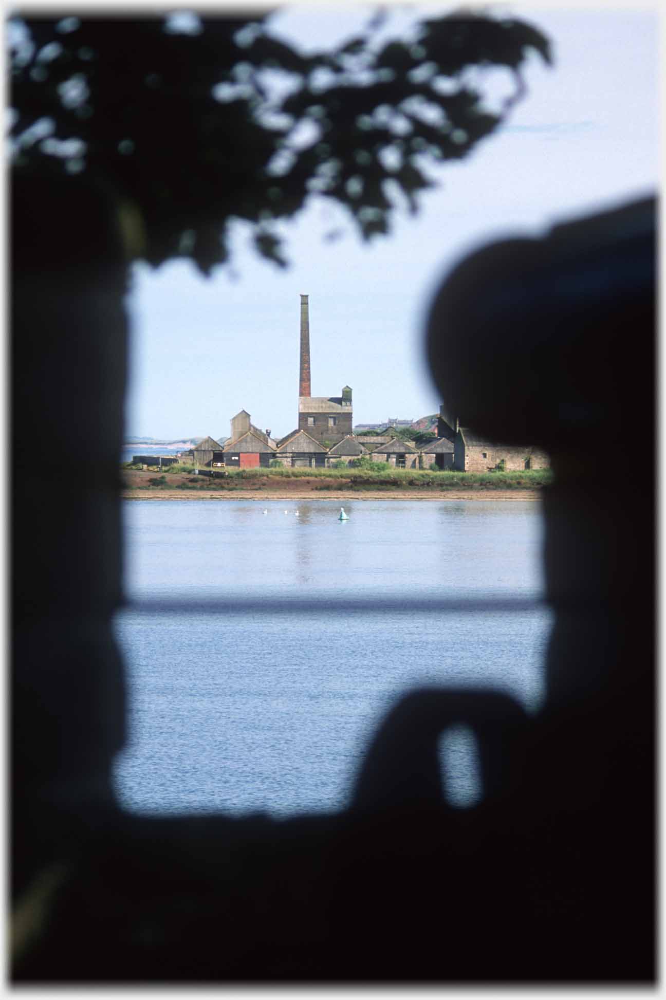 Outline of cannon framing buildings and chimney across water.