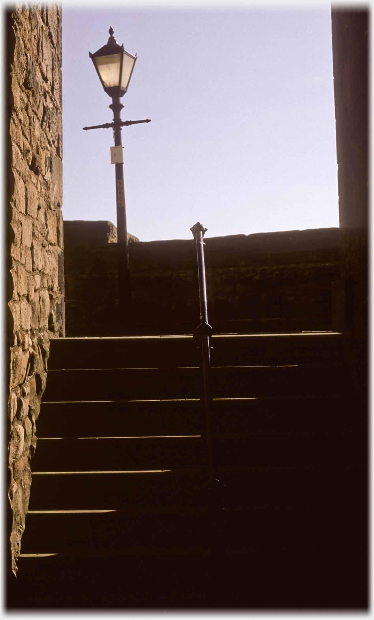 Light catching side of steps with post, parapit and lamppost.