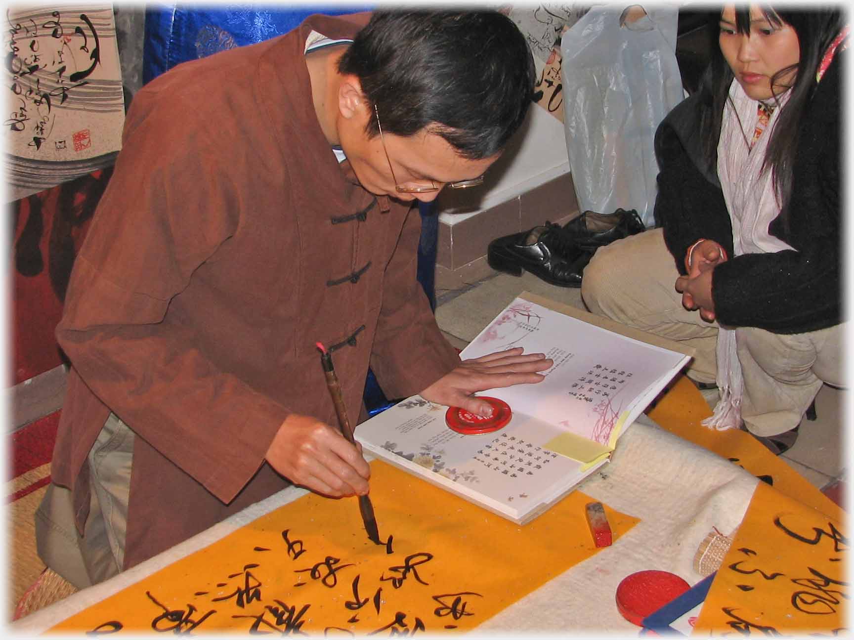 Man in brown tunic writing character.