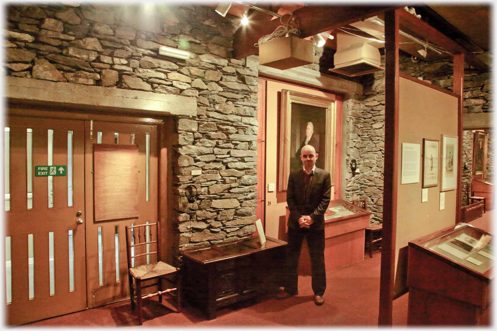 Man standing  in area with plain stone walls.