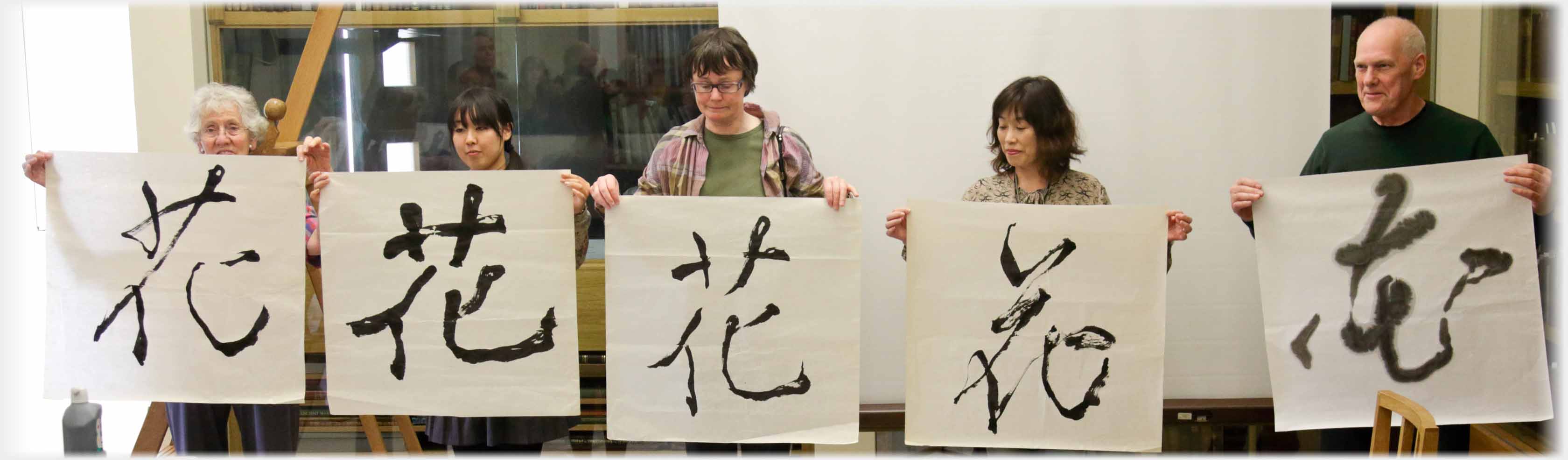 Five people in line each holding large sheet of paper with a character on it.