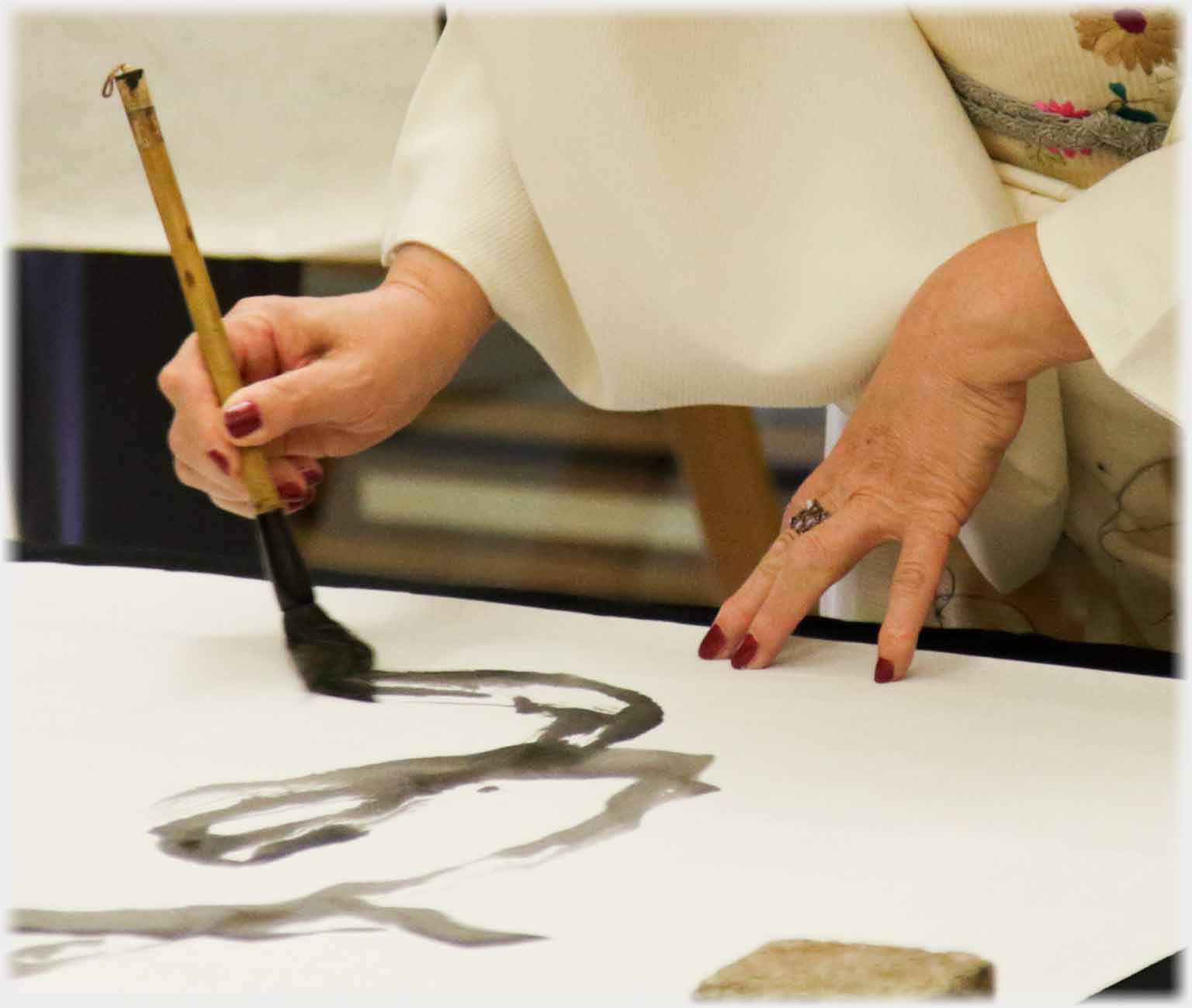 Hand holding down paper and hand writing with brush.