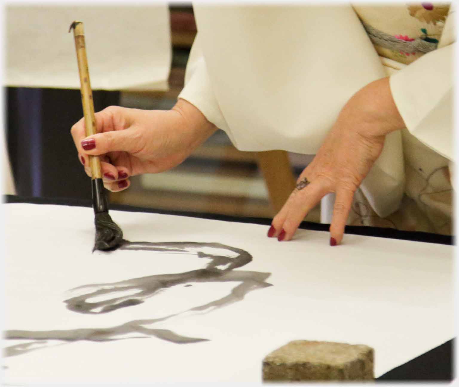 Hand holding down paper and hand writing with brush.