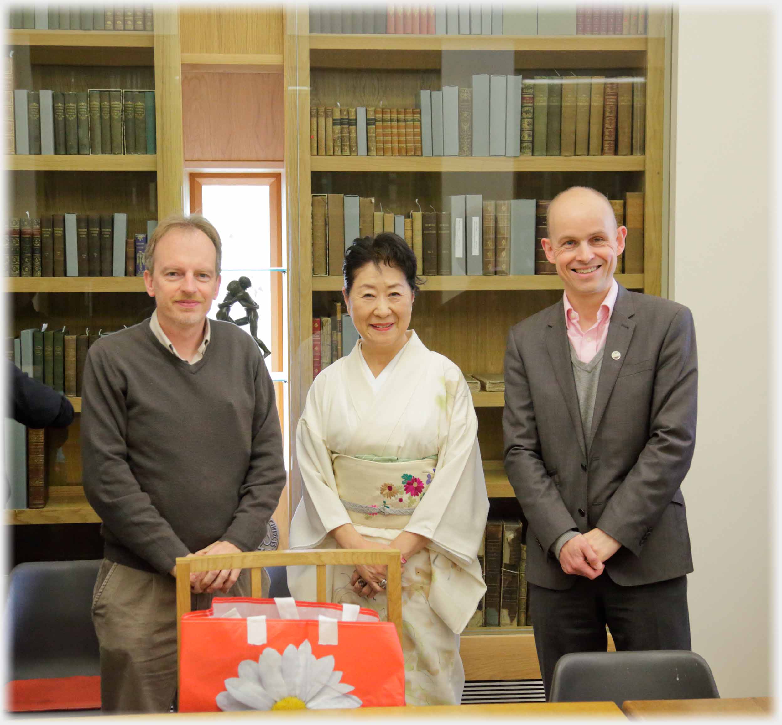 Two men on either side of kimono clad woman, books behind.