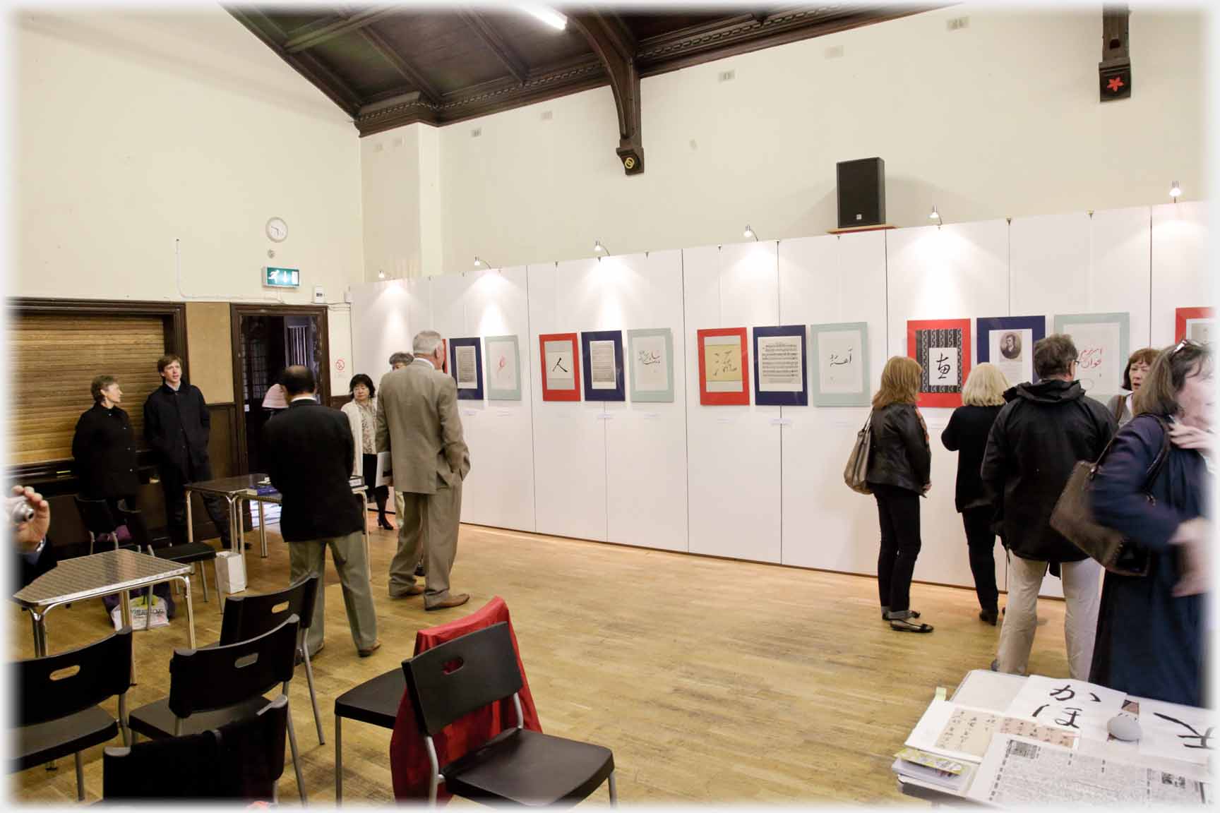 Room with line of pictures on while wall and people milling.