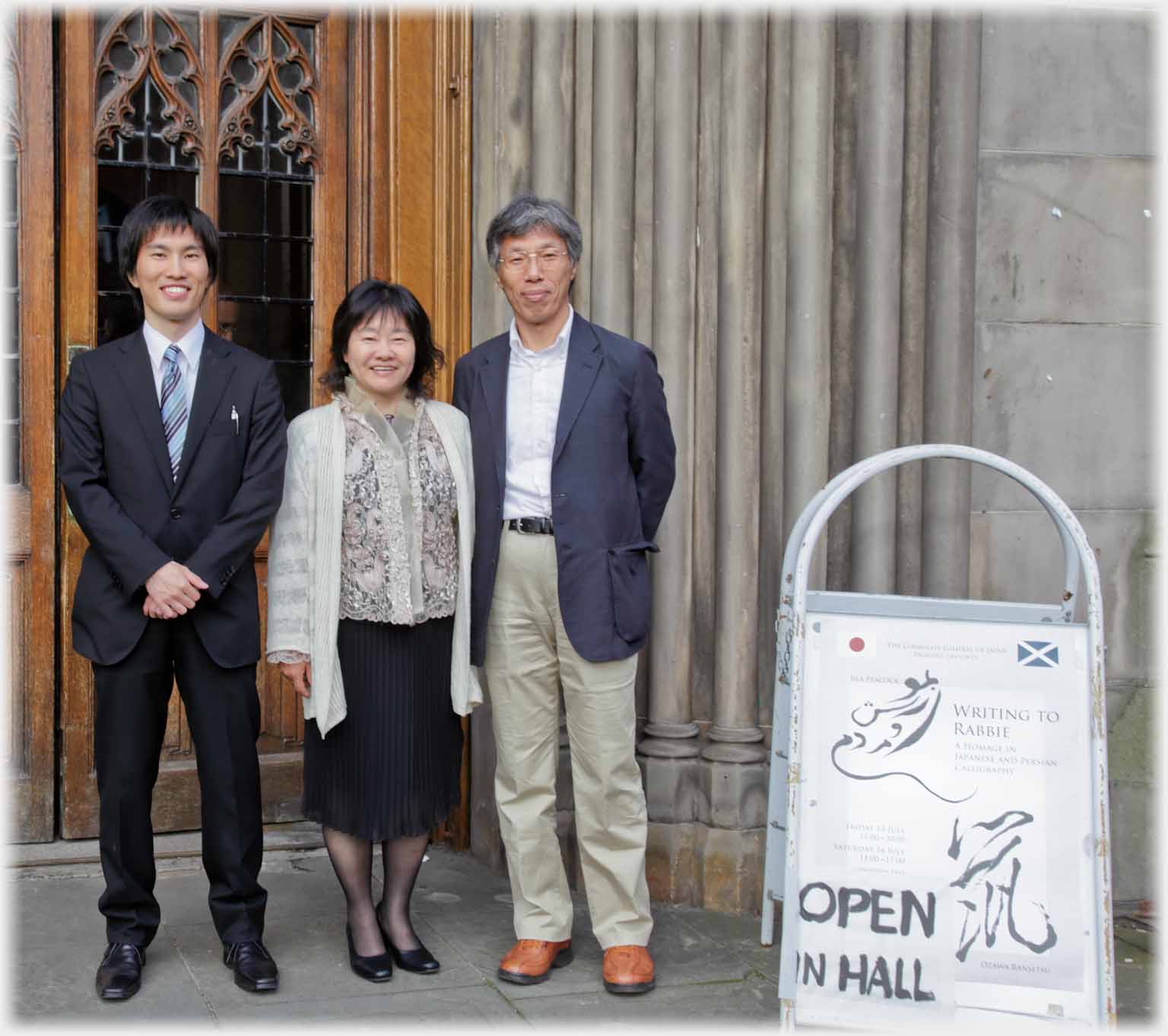 Japanese couple with younger man standing at church door by poster.