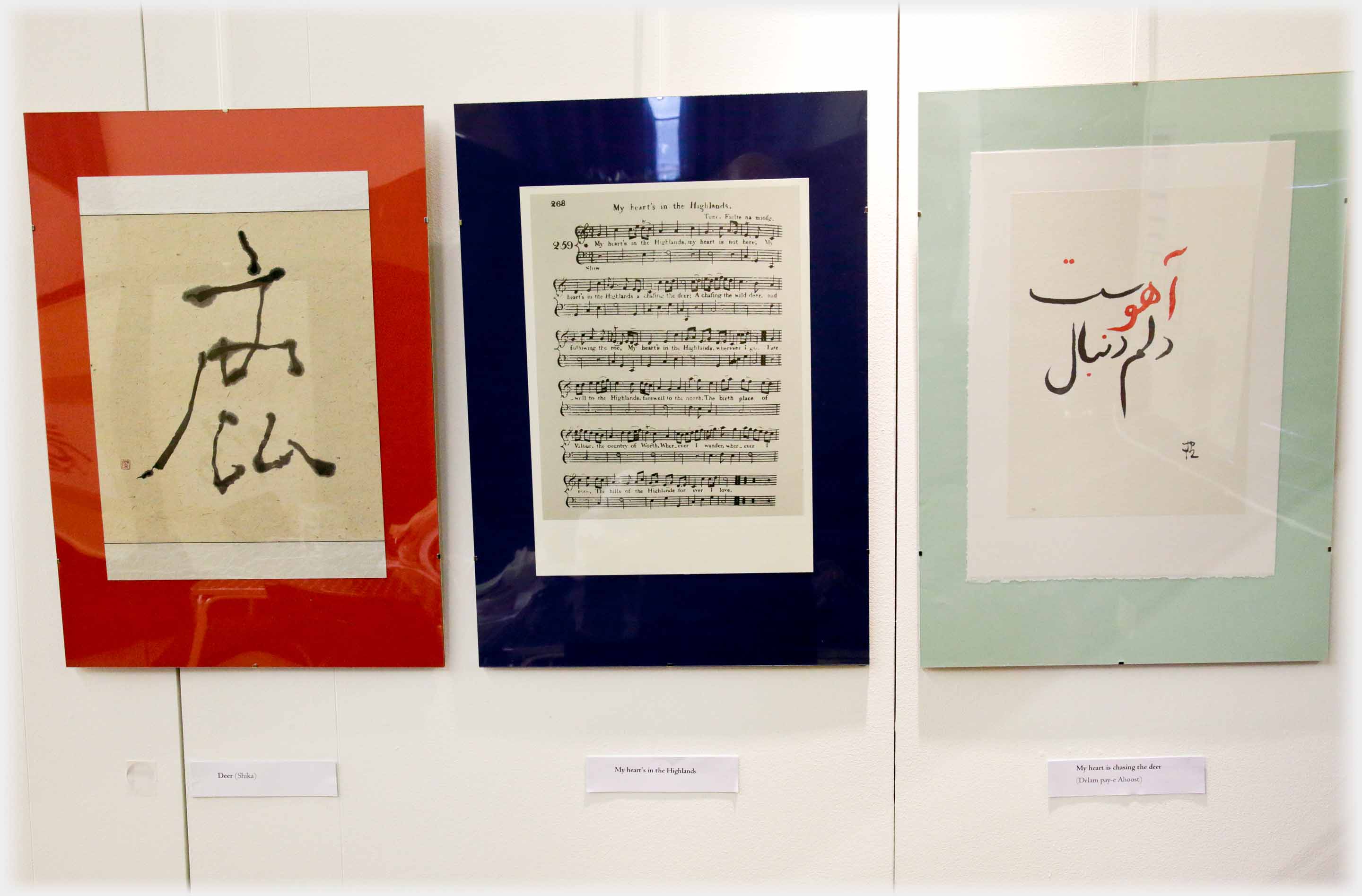 Three hung panels: left Japanese calligraphy, centre sheet of music, right Persian writing.