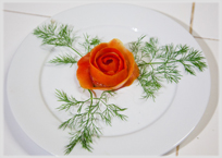 White plate with carrot cut aas rose and three carrot fronds.